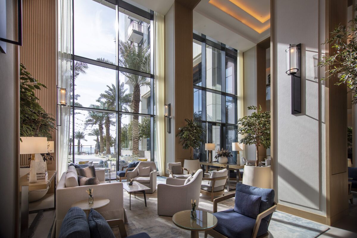 Hall d'entrée d'un hôtel luxueux avec une grande façade en verre, donnant sur un jardin avec des palmiers.