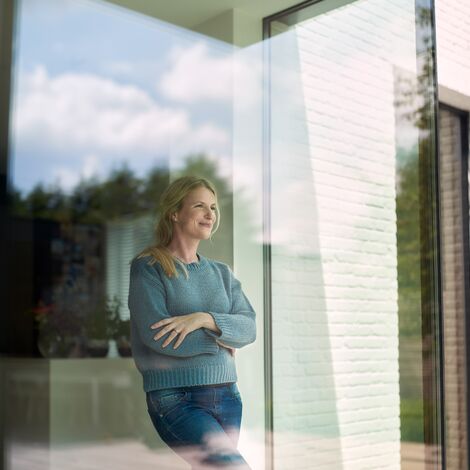 Vrouw kijkt tevreden naar buiten door een groot Reynaers Aluminium raam