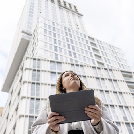 Femme blonde tenant un iPad regardant vers l’immeuble d’appartements blanc.