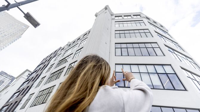 Femme levant les mains vers un immeuble blanc de taille moyenne avec beaucoup de fenêtres.