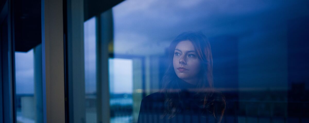 Femme regardant par la fenêtre à la tombée de la nuit.